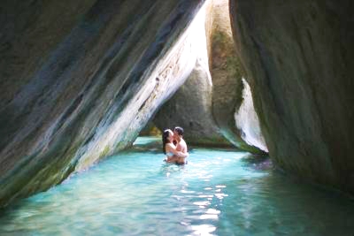 Couple kissing in water below huge boulders