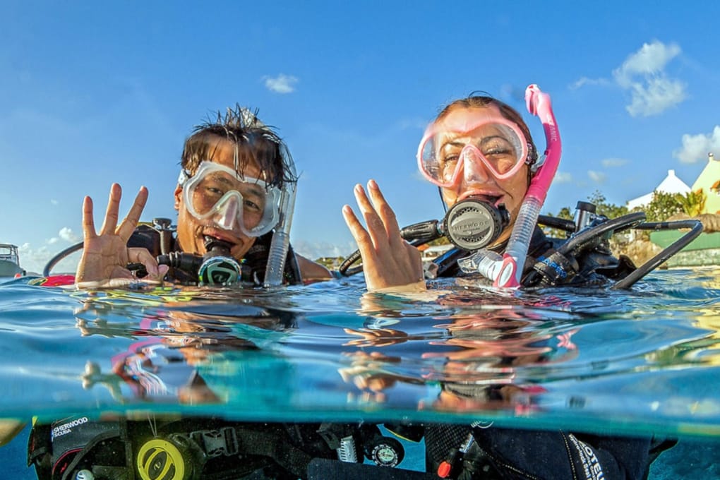 Couple with scuba diving gear in water waving